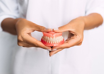 Woman wearing white holding full set of dentures with both hands