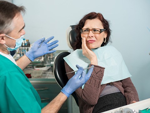 A woman frowning and touching her cheek while looking at her dentist