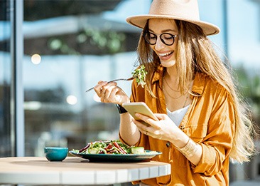 Smiling woman eating lunch and looking at her phone outside