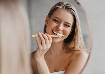 Woman smiling while brushing her teeth at home