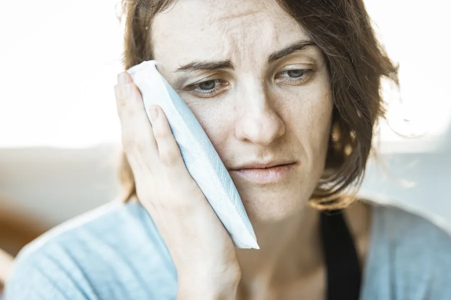 Person holding a cold compress to their swollen cheek from dental pain